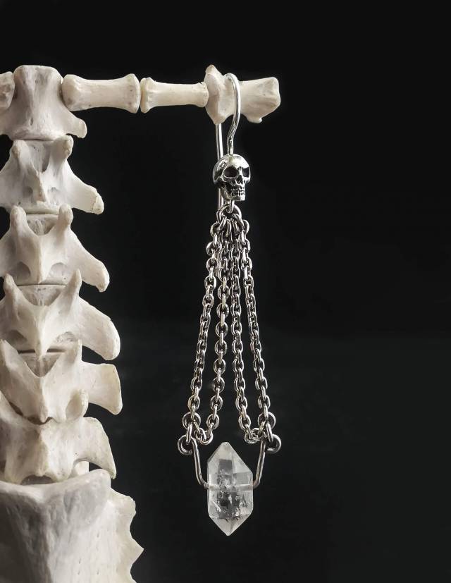 Close up of a dainty skull earring with clear crystal gemstone and chains.