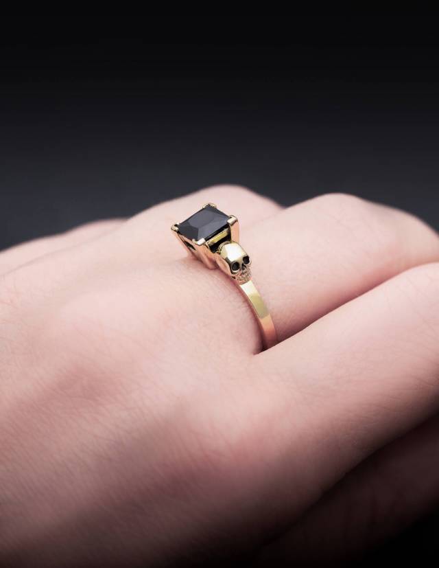 Solid gold two skull ring Thyone with black diamond shown on a hand.